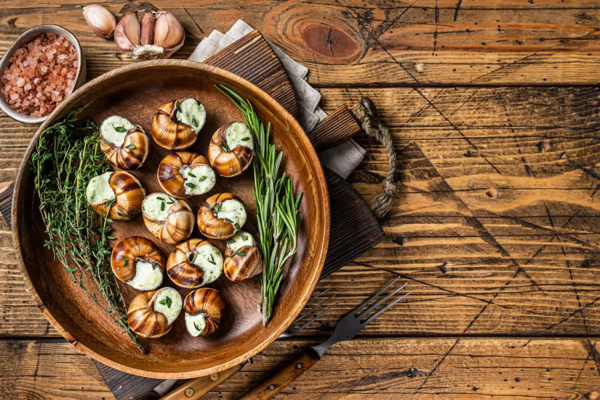 Succulent escargot smothered in garlic herb butter, presented in a wooden dish with fresh herbs.