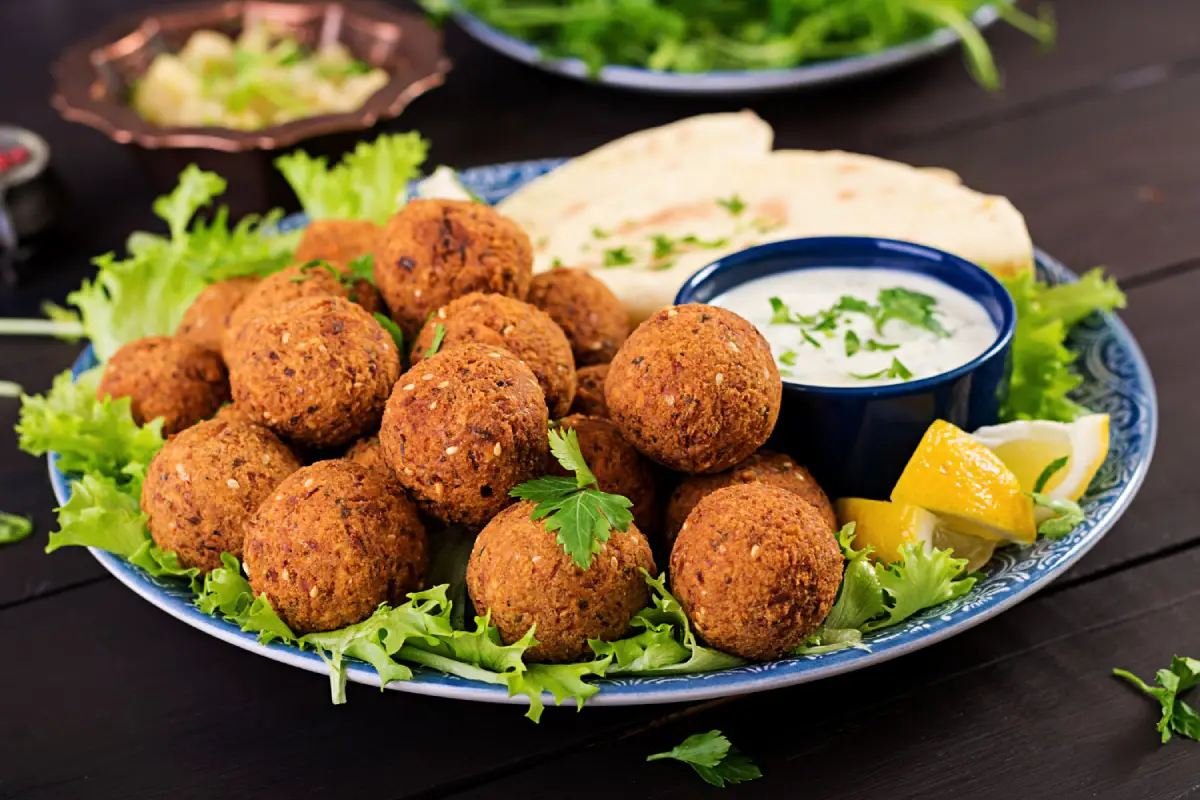 A decorative plate piled with crispy homemade falafel balls, garnished with parsley, served with pita bread, lemon wedges, and a bowl of tahini sauce.