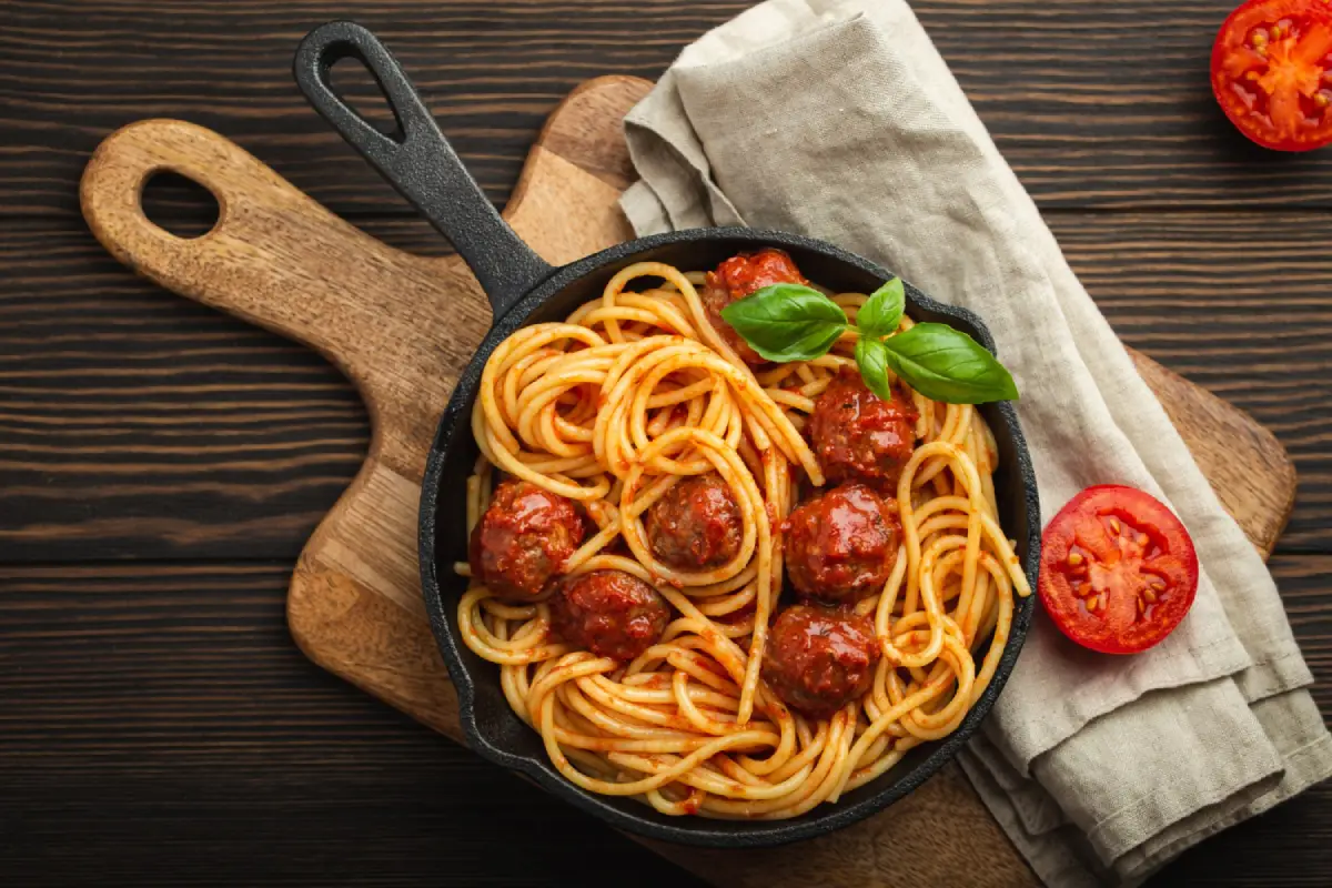 Spaghetti with meatballs and basil in a cast-iron pan, ready to serve.