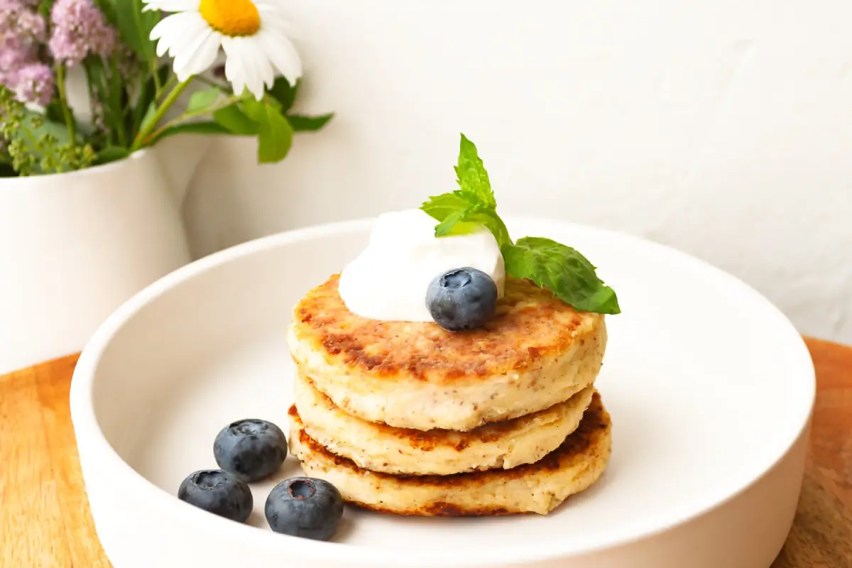 A stack of golden cottage cheese pancakes topped with a dollop of cream and fresh blueberries.