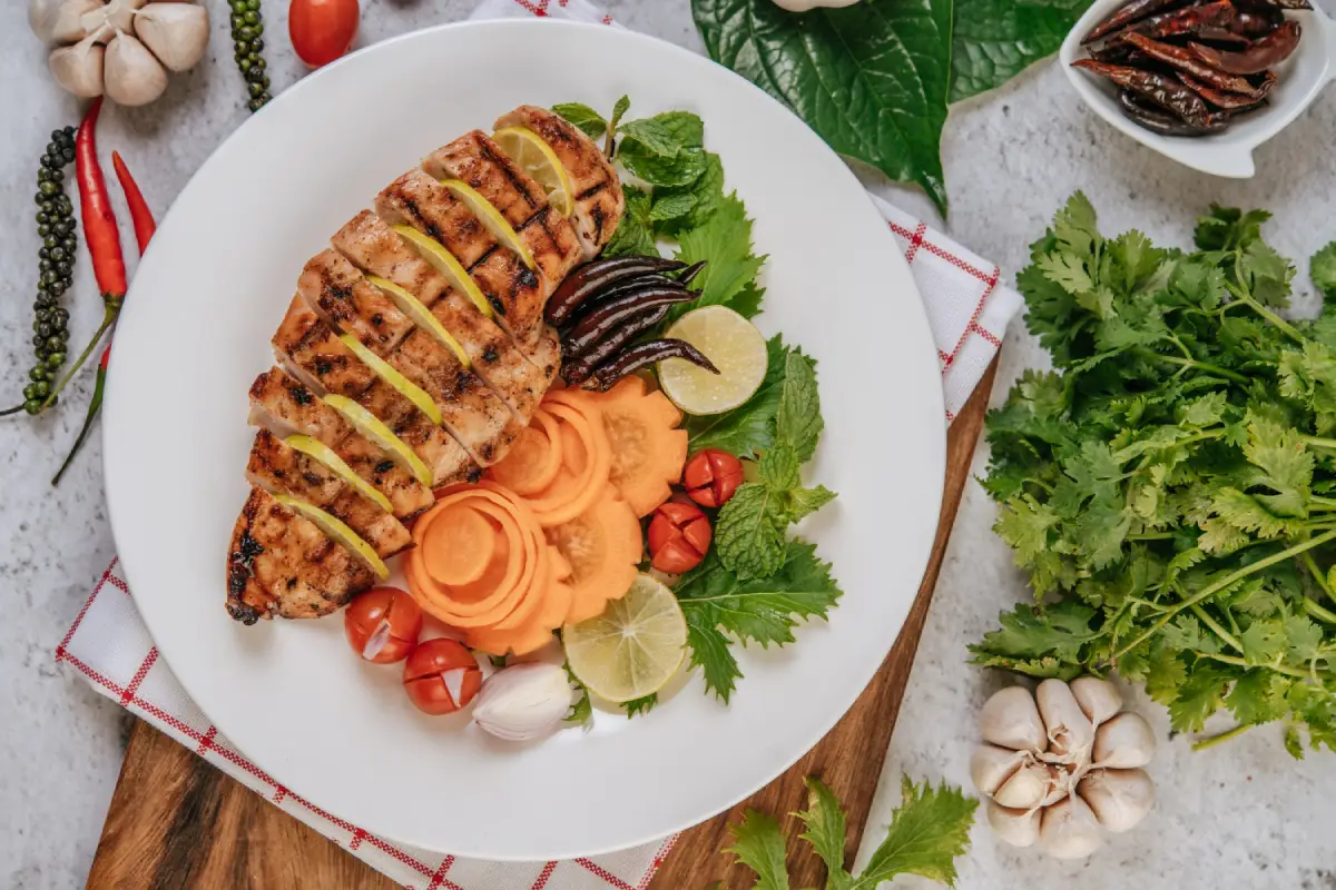 Grilled chicken breast sliced on a white plate with fresh herbs and vegetables.