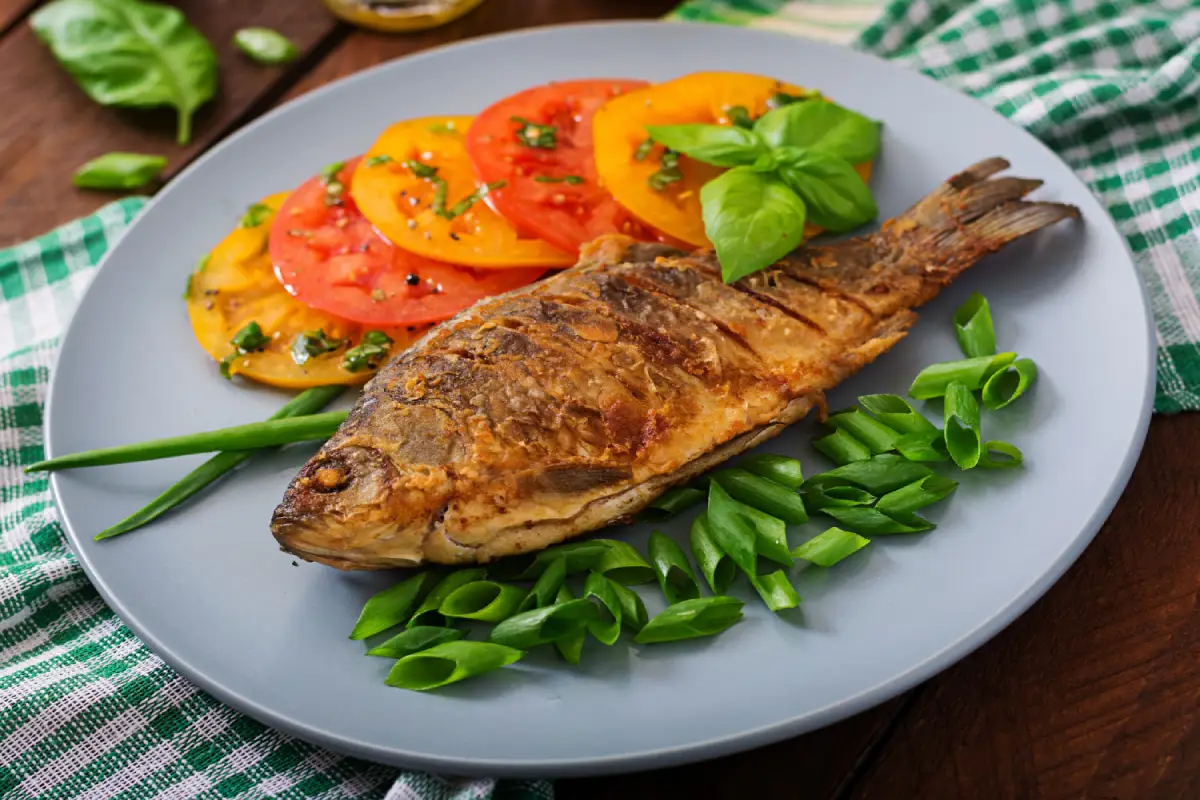  Grilled fish alongside a colorful tomato and basil salad on a gray plate.