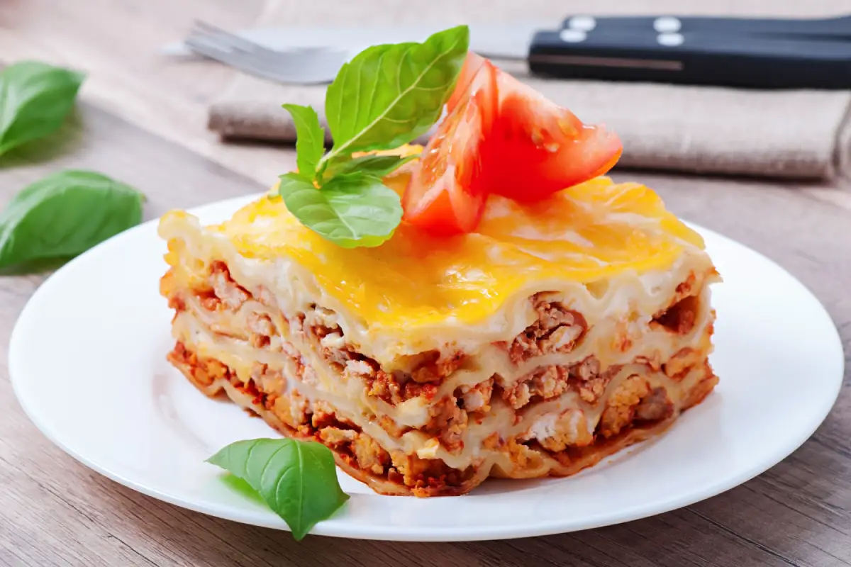 A piece of homemade lasagna with bolognese sauce, melted cheese, and fresh basil on top.