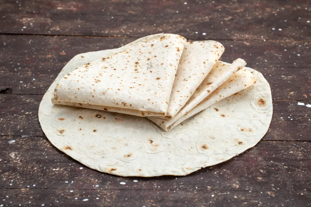 Freshly made pita bread stacked on a rustic wooden table, showcasing the soft texture and traditional pockets.
