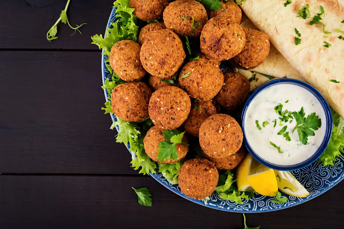 An inviting platter of crispy falafel garnished with parsley alongside pita bread and a bowl of tahini sauce, ready for serving.