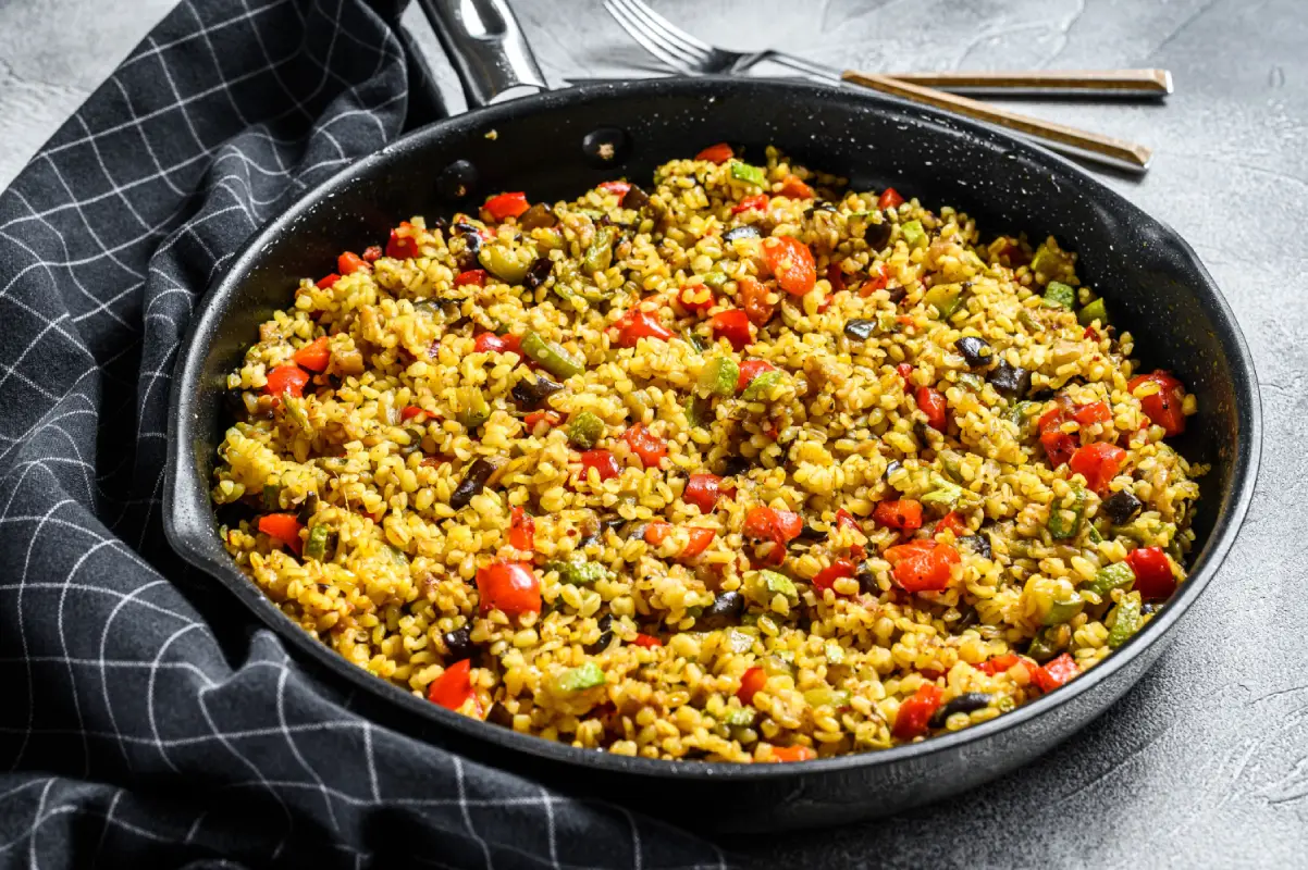 Aromatic bulgur with mixed vegetables served on a matte black plate, ready to enjoy.