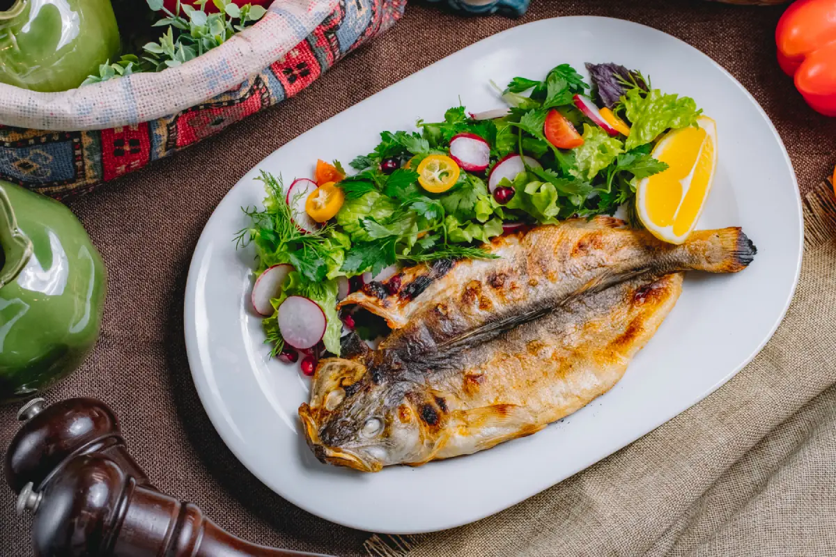 Grilled whole fish on a white oval plate with a mixed greens salad and lemon wedge.