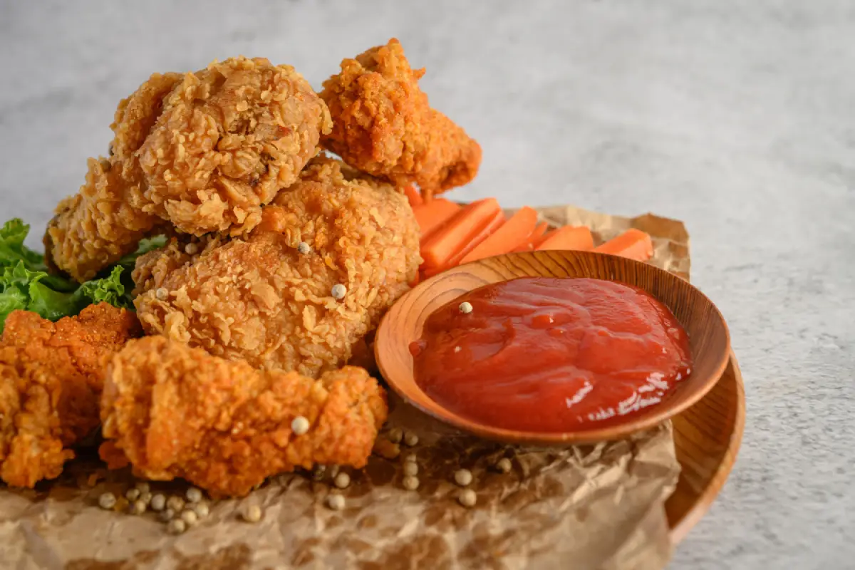 Close-up of a mouthwatering fried chicken meal, served with crisp carrot sticks and a smooth tomato sauce on a traditional plate.