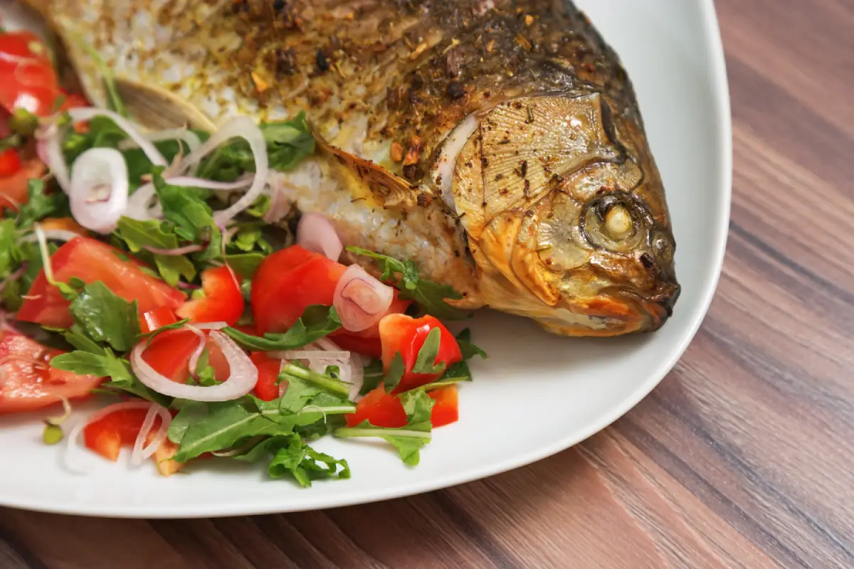 Close-up of a herb-crusted fish head with a colorful side salad on a white plate.