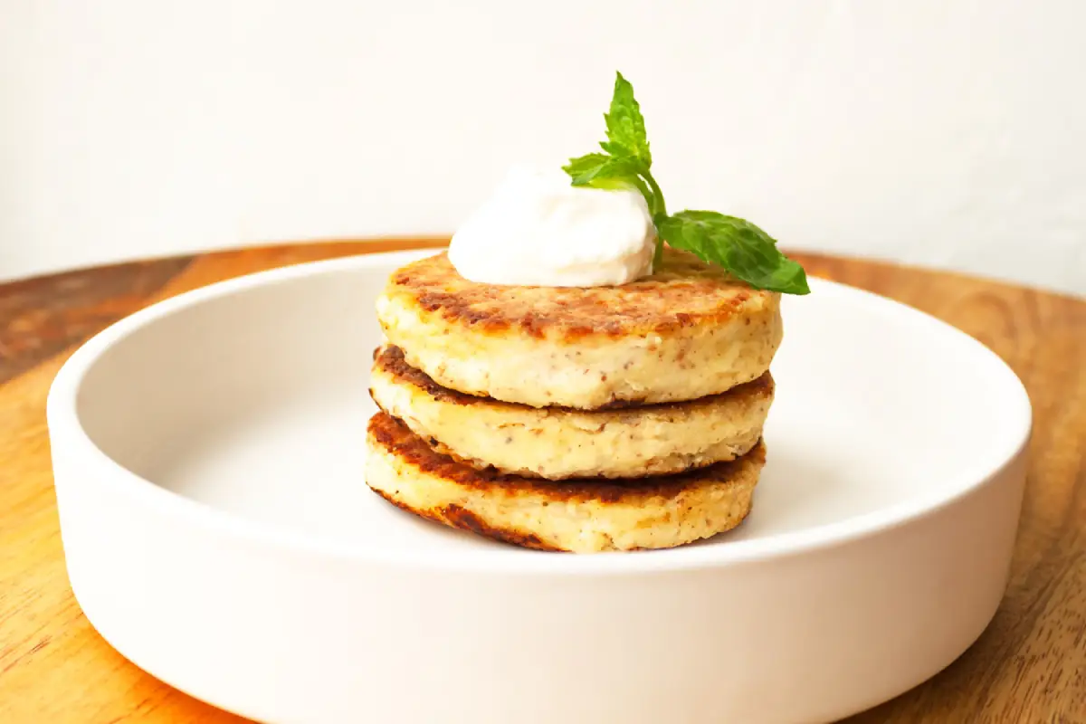 Warm cottage cheese pancakes with a dollop of whipped cream and a mint leaf on top, served on a circular white plate.