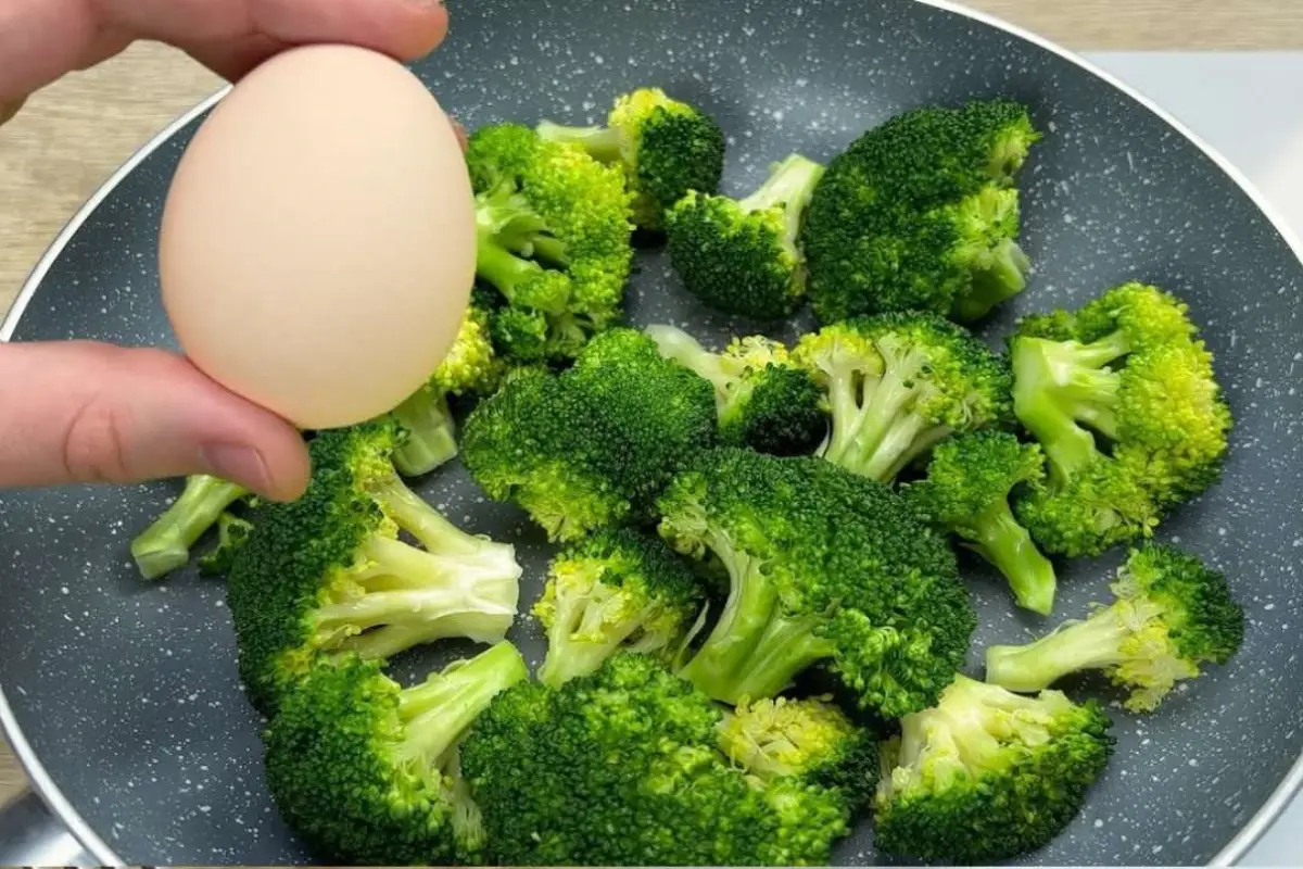 Fresh egg held over a pan of bright green broccoli florets, prepping for a Healthy Broccoli Egg Bake.