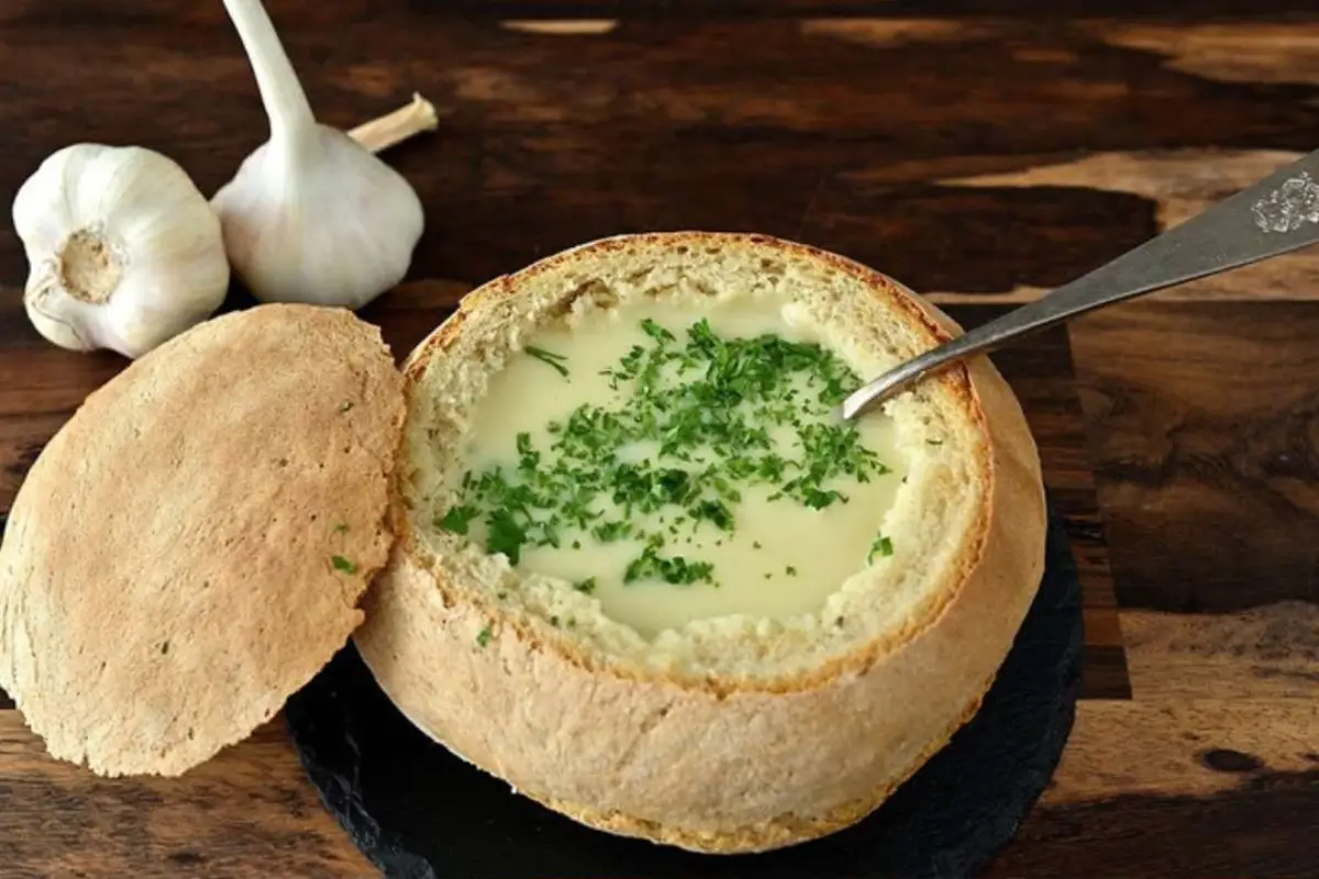 Authentic Austrian Garlic Soup garnished with parsley in a freshly baked bread bowl.